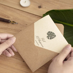 Person holding a brown envelope with a leaf design on a wooden surface