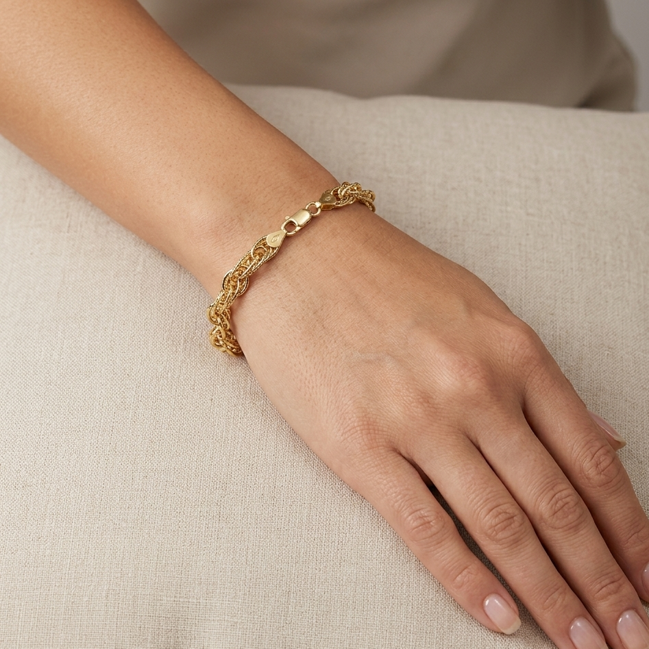 Gold bracelet on a person's wrist against a neutral background