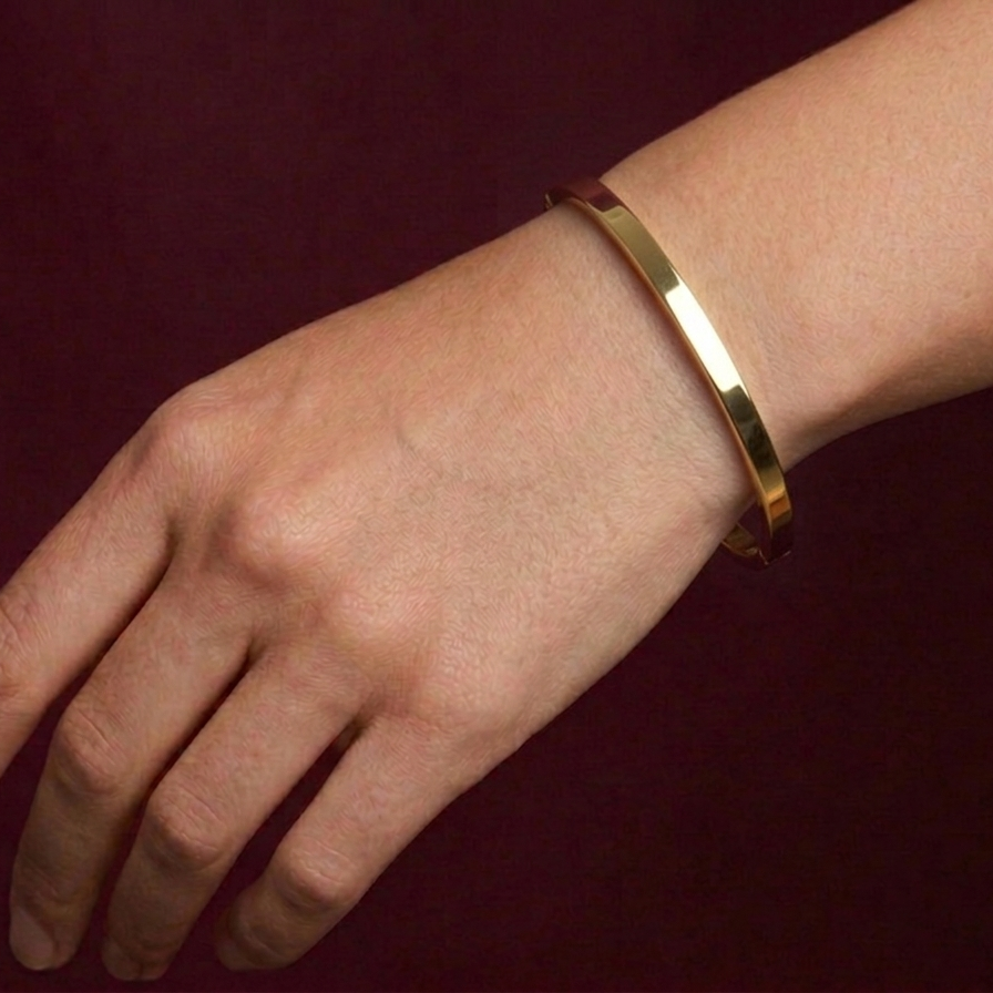 Gold bracelet on a wrist against a dark background