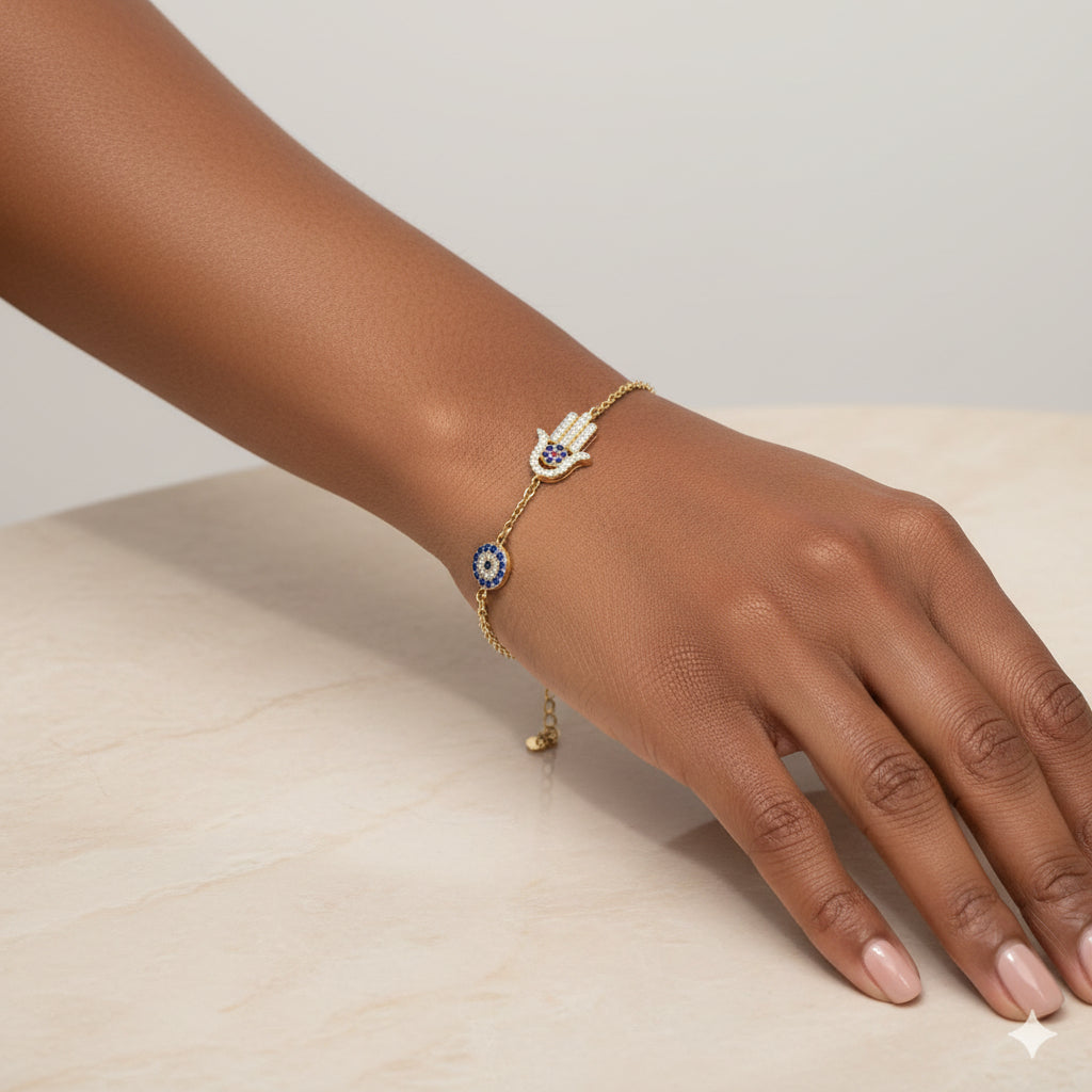 Gold bracelet with hamsa hand and eye charm on a maroon background